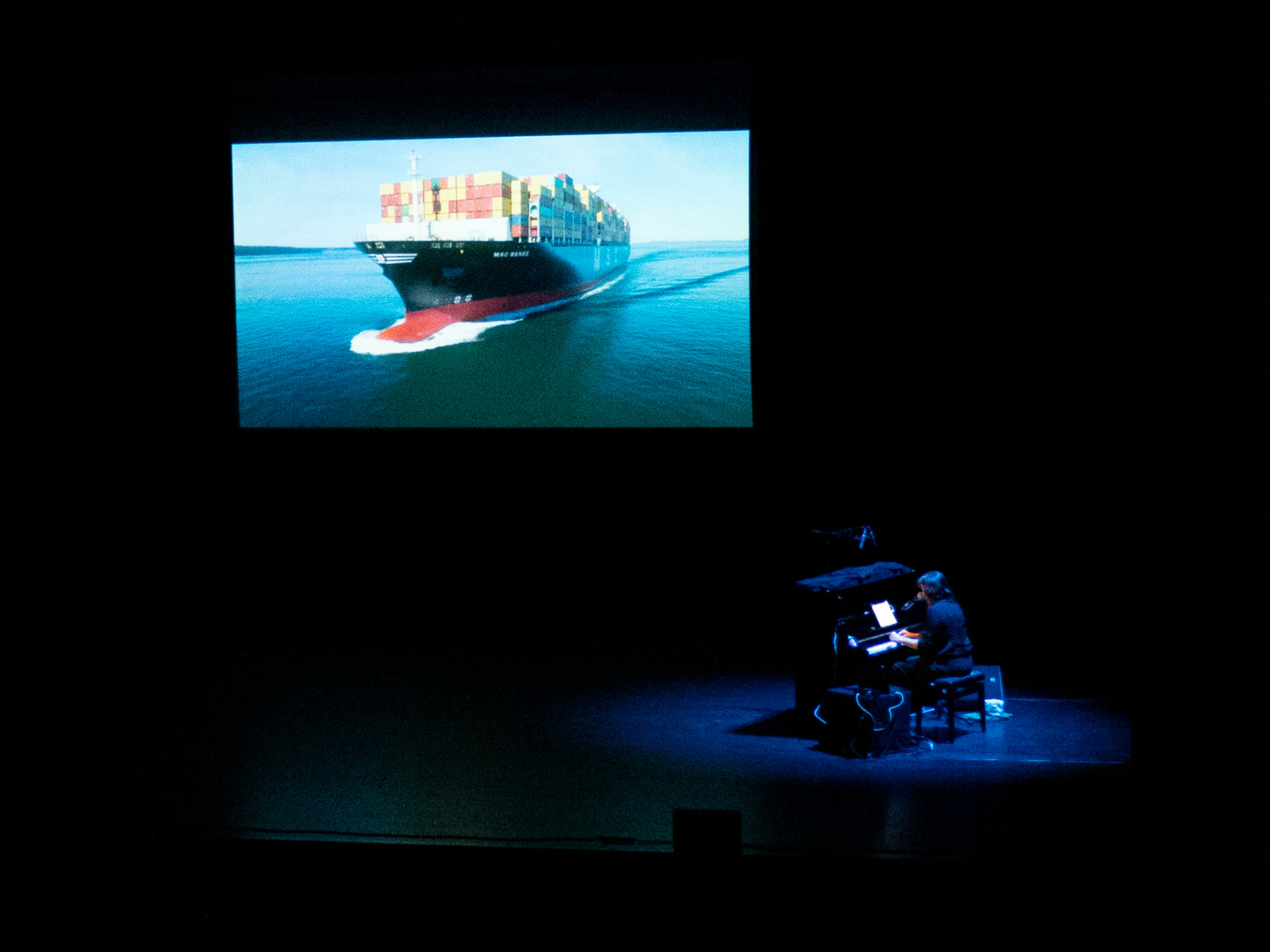 Pianiste sur scène sous une projection de porte-conteneurs